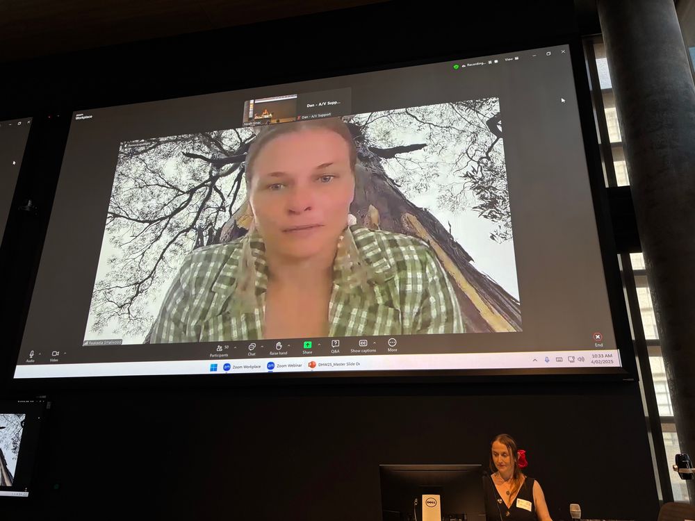 Large Zoom screen showing Rakeeta during her Acknowledgement of Country, in the room is conference co-chair Anna Janssen