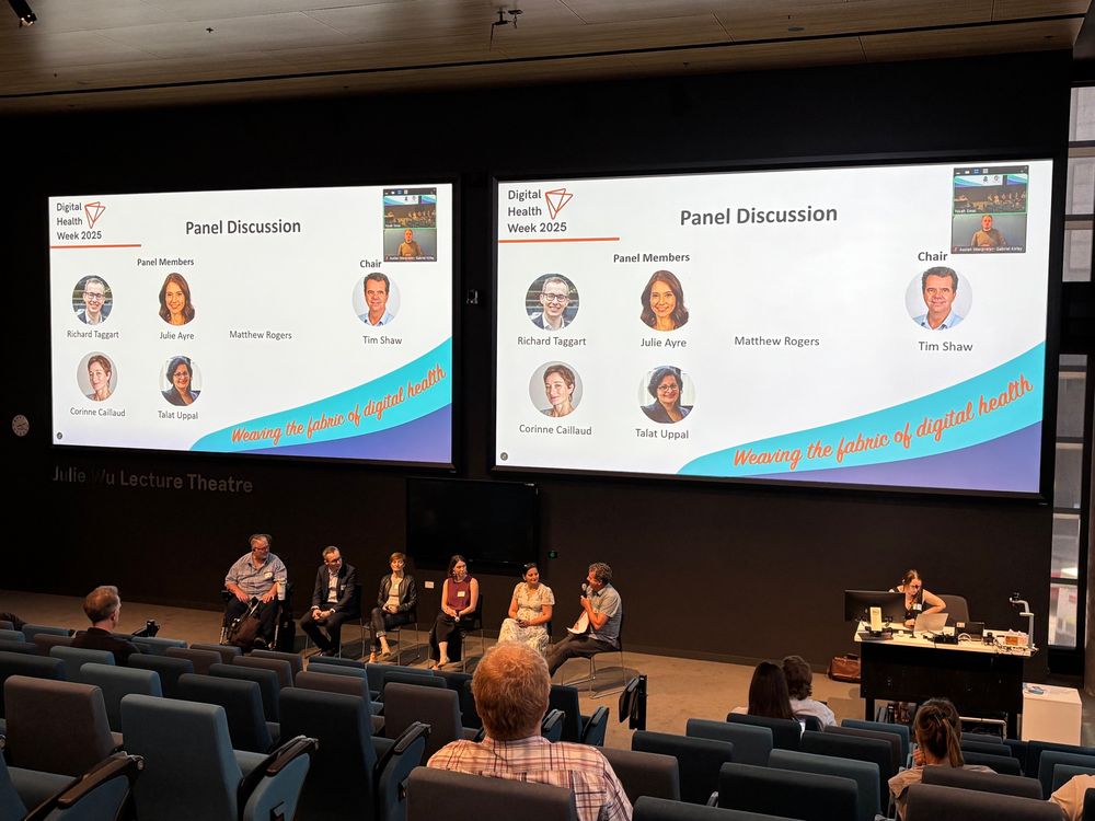 Photo of panel members speaking at Digital Health Week 2025, their names are shown on the big screen