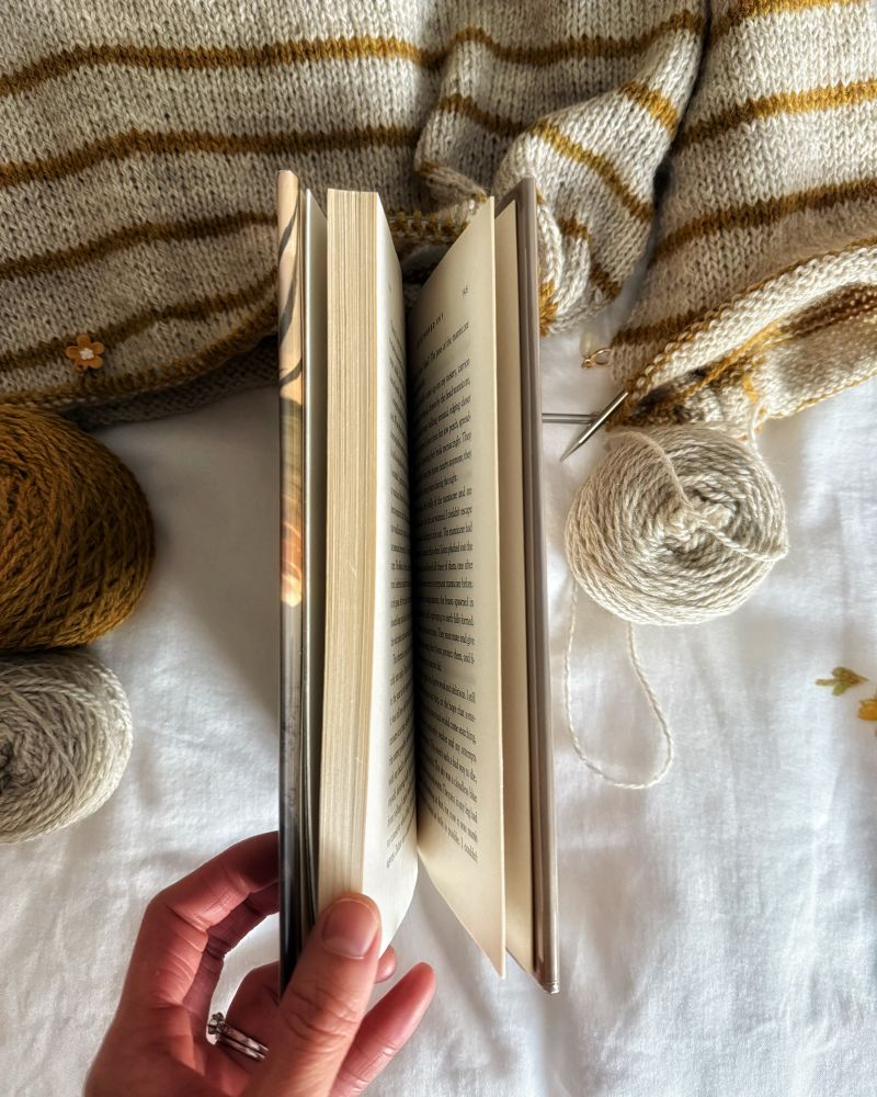 Side of hardcover book held slightly open by tan skin hands. 