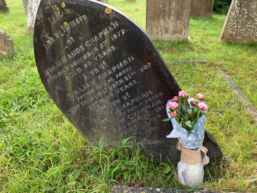 A toppled gravestone from the very early 20th century, with a fresh bunch of pale pink peonies placed at its foot