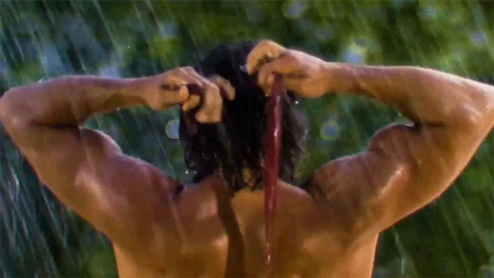 a shirtless man is standing in the rain holding his hair in a ponytail