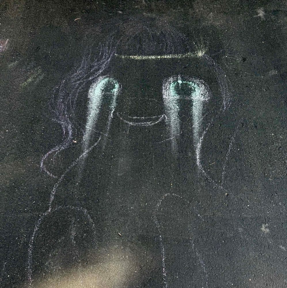 A chalk drawing of a my little pony on a driveway. The chalk around the eyes has run like goth/emo makeup. 