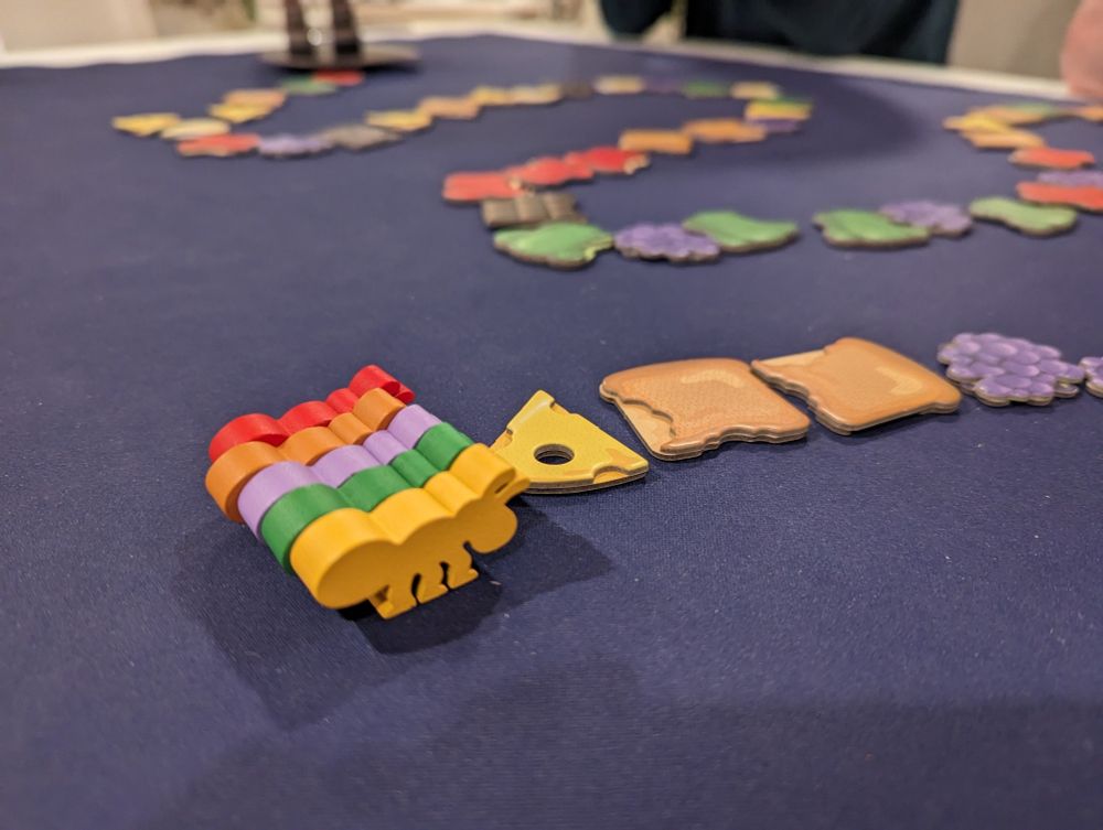 5 wooden ants line up before a twisting path of food-shaped playing pieces matching the 5 colors of the ants.