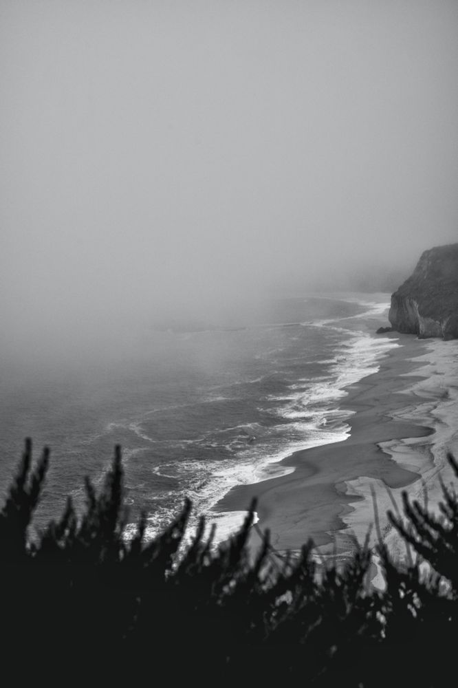 Pic in black and white of a stormy sea view with waves thrashing over a sandy cove