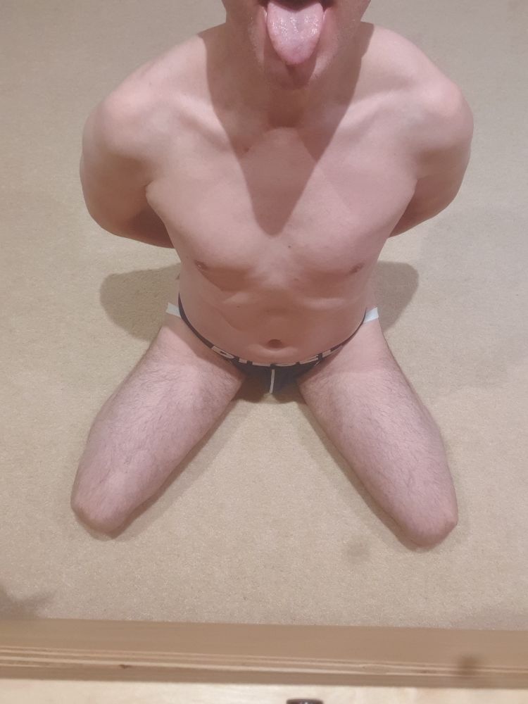 I'm on my knees, legs apart, hands behind my bank, wearing nothing but a jock, with my mouth open and my tongue out
