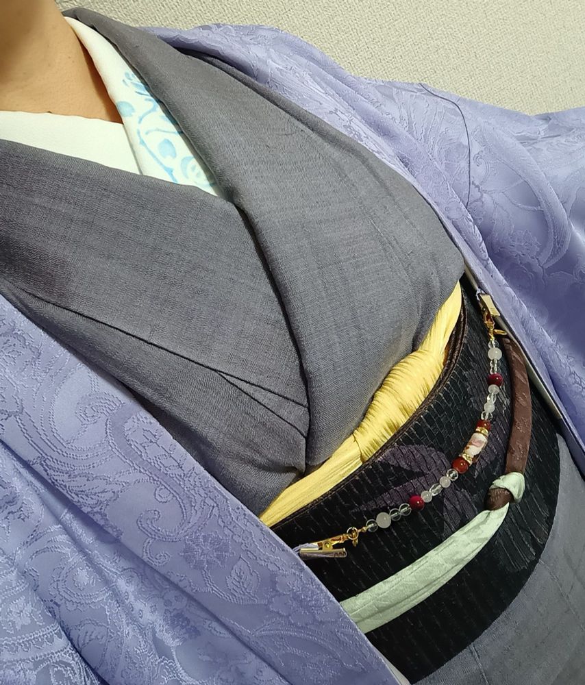 半衿は型染体験で作ったもので、青いバラが左側の前面に入っている。パープルよりのグレーの紬。箔の入った黒地の帯。帯揚げは錦糸卵みたいな黄色で、帯締めは茶色とピスタチオみたいな色のバイカラーでラメ入り。羽織は薄い紫色でペイズリーの地模様。羽織紐はピンク系のビーズ。