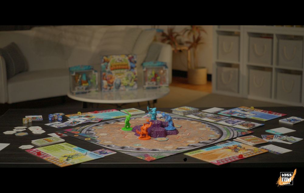 A photo of a living room with the Saurozoic Warriors board game laid out on a table.  The arena board has colorful miniatures on it, with cards laid around.