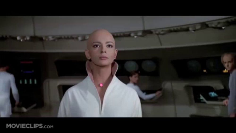 a woman with a bald head is standing in a room with movieclips.com on the bottom