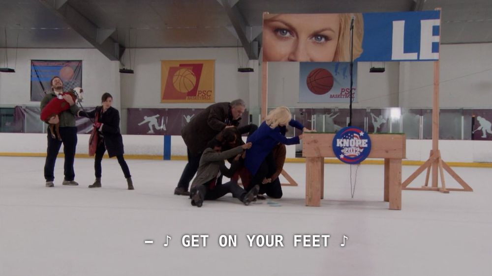 screenshot from the parks and rec episode where leslie and co are slipping on an ice rink because the carpet wasn't long enough to reach the podium for her speech, with "get on your feet" playing in the background