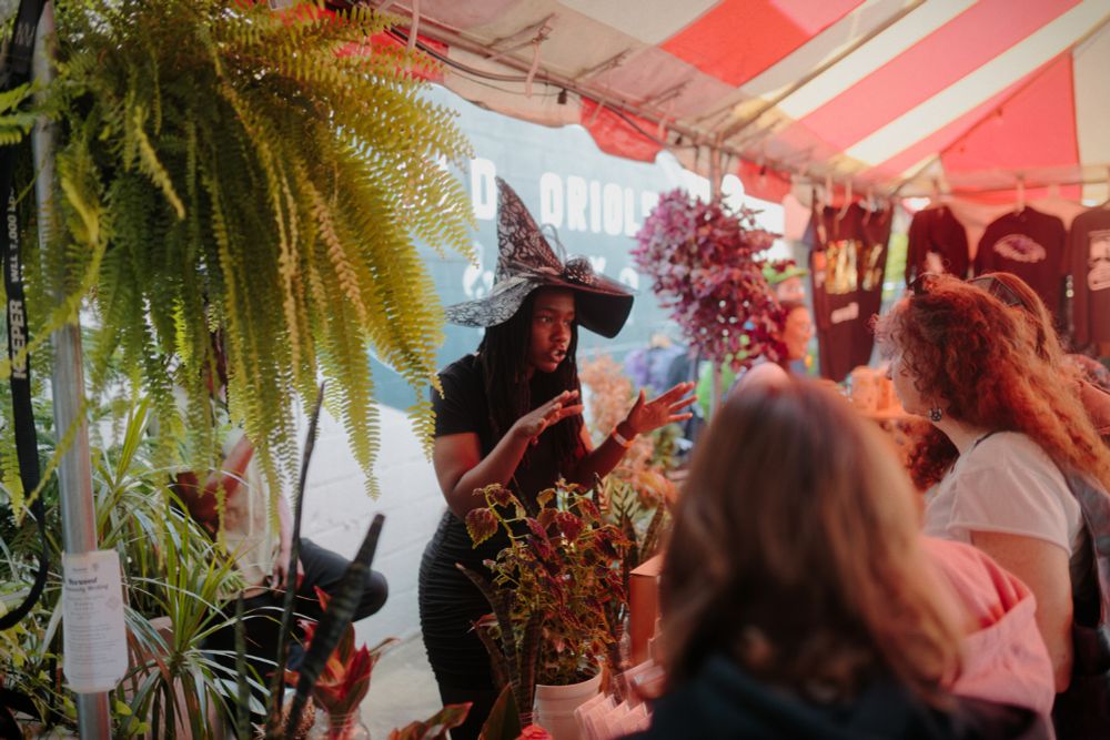 A woman in a witch costume shows her crafts to a crowd at a Halloween market.