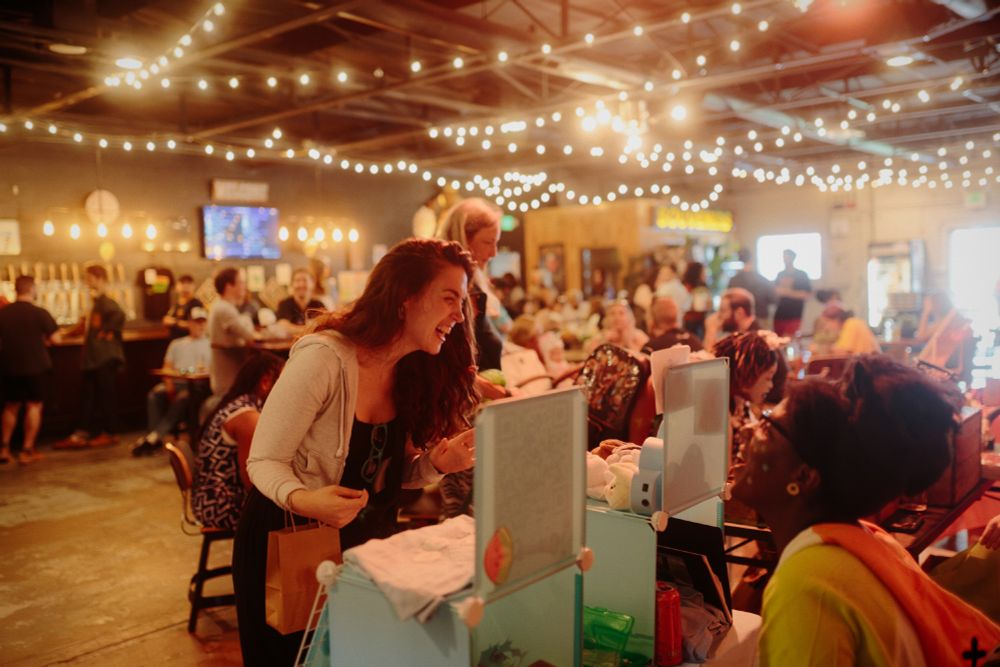 Women laughing in a brewery hall lit by string lights.