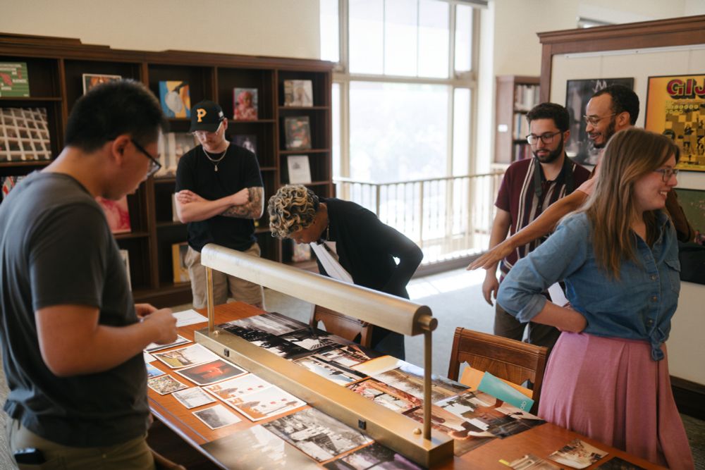 People examining photographic prints on a library table.