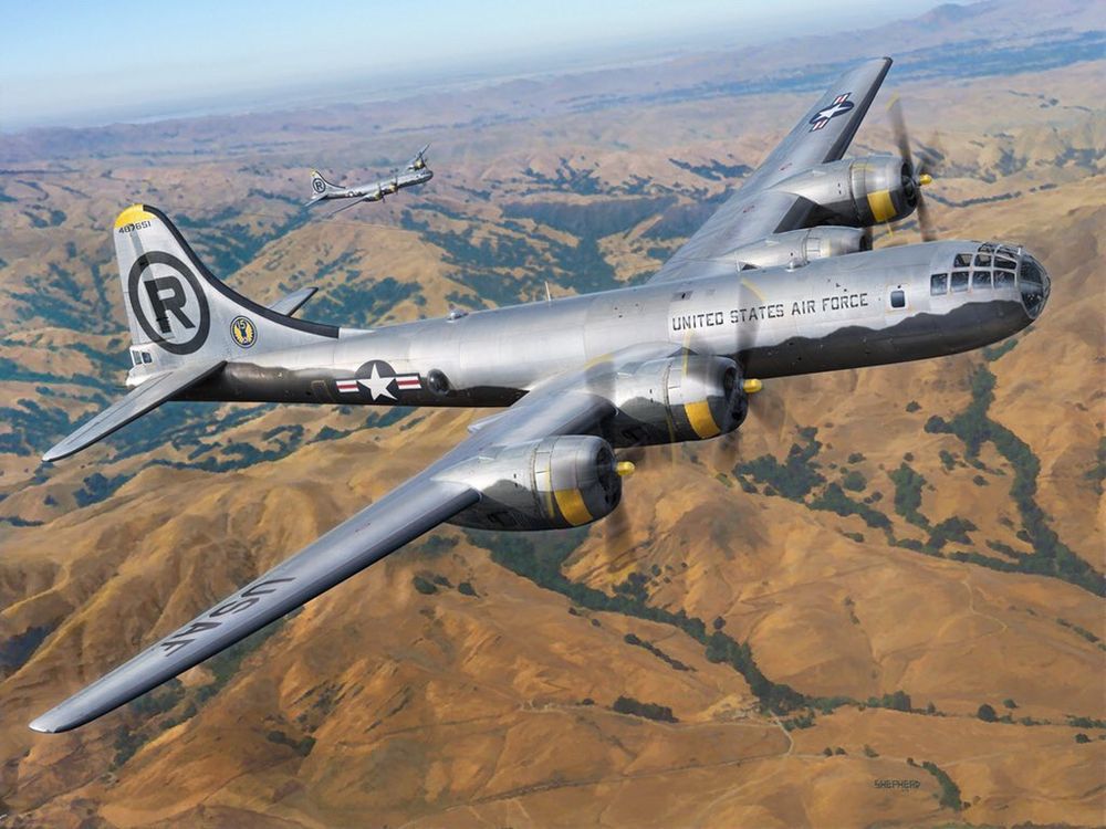 A color photograph of two B-29 bombers in flight over dry, hilly terrain, one very large in the foreground and one much smaller in the background.
