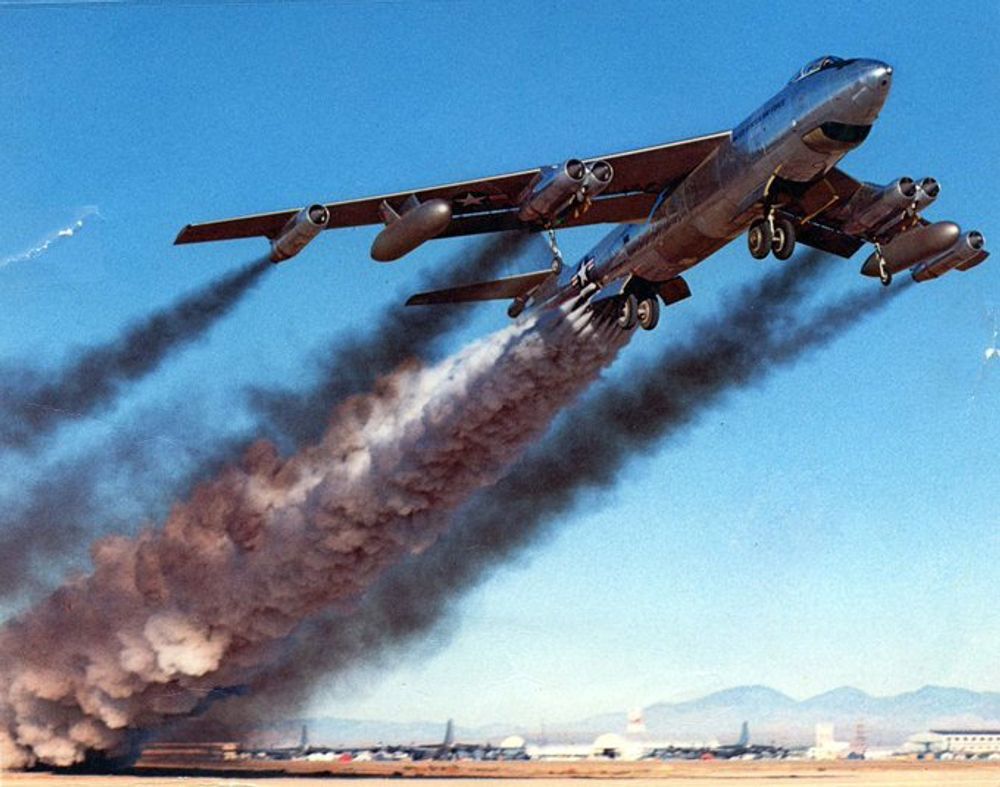 A color photograph of a B-47 bomber taking off using multiple Jet-Assisted Take Off rockets (JATO) attached to the aft fuselage. Large plumes of smoky exhaust pour from the six jet engines and the rockets.