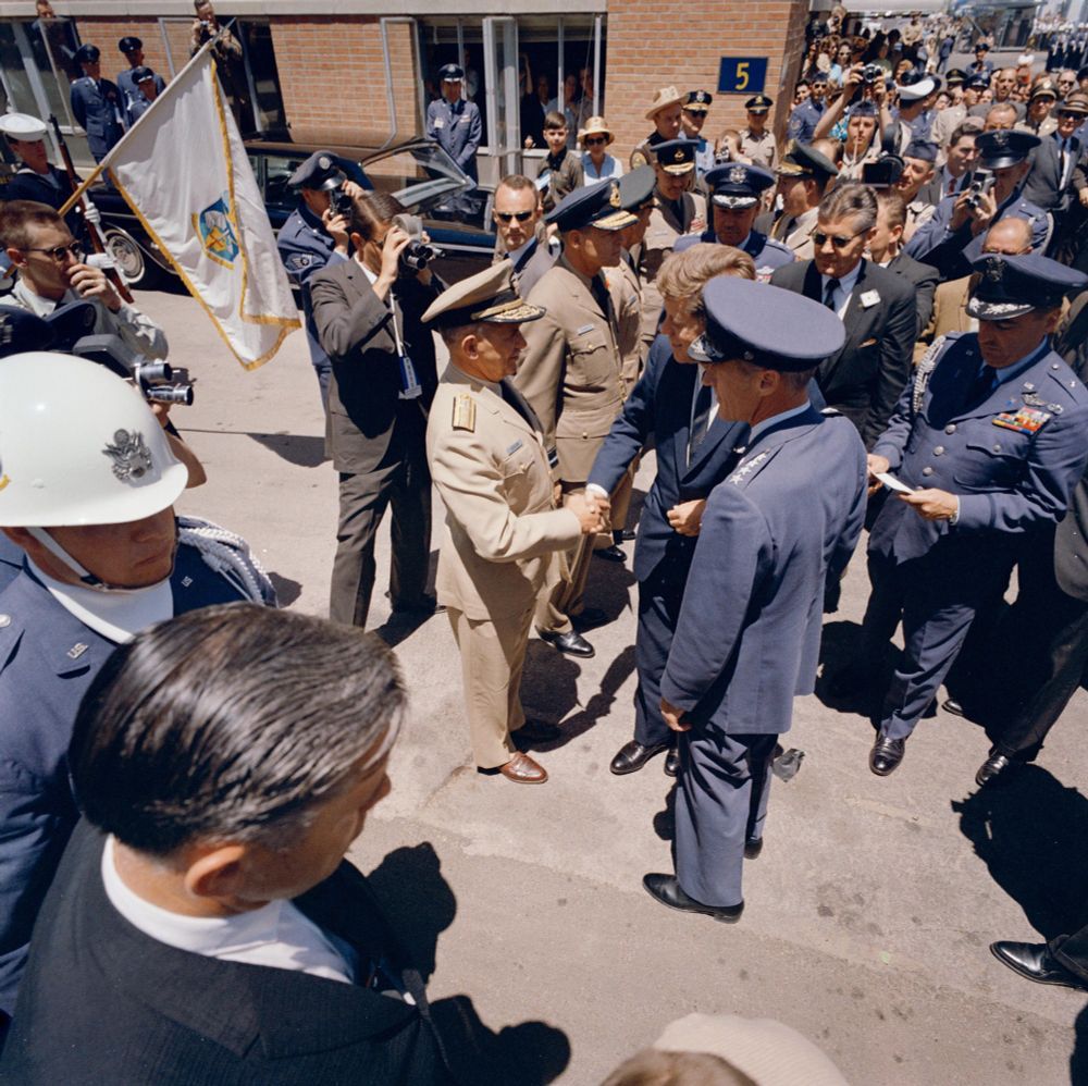 An official color photograph showing President John F. Kennedy (center) shaking hands with Chief of the Air Staff of the Royal Canadian Air Force (RCAF), Air Marshal Clarence R. Dunlap, during his visit to NORAD headquarters at Ent Air Force Base in Colorado Springs, Colorado; Commander of NORAD, General John K. Gerhart, stands to the right of President Kennedy. Also pictured: Air Force Aide to the President, Brigadier General Godfrey T. McHugh; Deputy Commander of NORAD, Air Marshal Charles Roy Slemon (RCAF); Vice Commander of the Air Defense Command, General Robert Merrill Lee; Military Aide to the President, General Chester V. Clifton; Special Assistants to the President, Kenneth P. O'Donnell, Larry O'Brien, and Dave Powers; and White House Secret Service agent, Gerald A. 