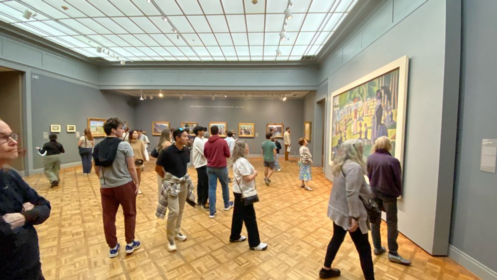 Gallery 240: visitors stand at varying distances to explore and admire Seuratβs large, colorful, and playful pointillist masterpiece βA Sunday on La Grande Jatteβ1884β.
