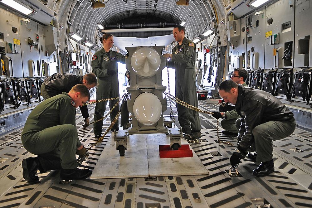 An official Air Force color photograph showing six airmen of the 62nd Airlift Wing strapping down a dolly containing two inert training versions of B-61 nuclear gravity bombs in a C-17 Globemaster on February 16, 2009. The 62nd Airlift Wing received top honors as the nation's Prime Nuclear Airlift Force after a week long inspection.