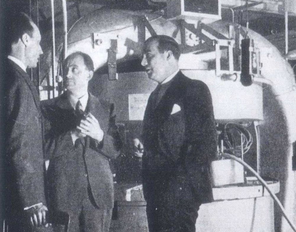 A black and white photograph showing (left to right) Dana Mitchell, Enrico Fermi, and John Dunning standing in front of the cyclotron at Columbia University in New York City.