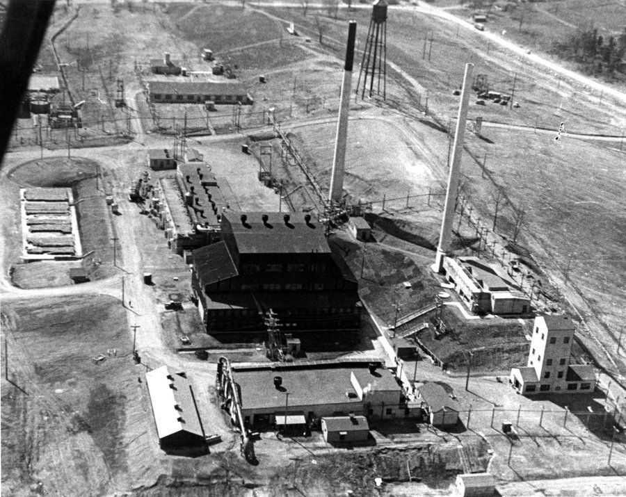 A low-level aerial black and white photograph of the X-10 reactor building at Oak Ridge, Tennessee, during World War II, surrounded by numerous smaller support buildings. 