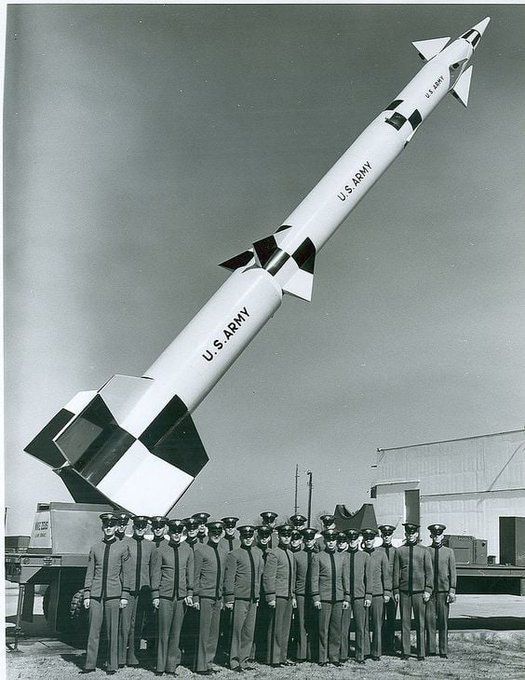 A black and white photograph of the large Spartan antiballistic missile on display on a truck (possibly at a test range). The black and white missile is pointed toward the sky while a medium-sized group of uniformed male Army personnel (cadets?) pose in front.