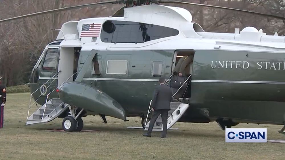 Screenshot from a C-SPAN video of the White House Military Office Marine Corps aide entering the rear door of Marine One on the South Lawn of the White House. He is holding the Presidential Emergency Satchel in his right hand. A Secret Service agent standing at the bottom of the stairs in a gray suit watches him board.
