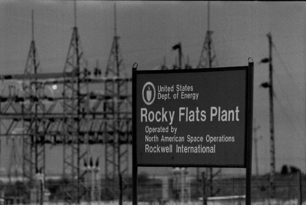 A black and white photograph of a large sign:

United States Department of Energy
Rocky Flats Plant
Operated by North American Space Operations
Rockwell International

In the background are power lines and electrical transformers.