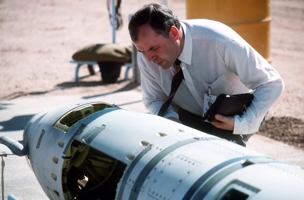 A color photograph of male inspector from the Soviet Union leaning over and carefully examining the nose section of a partially-dismantled US ground-launched cruise missile, whose deployment was banned by the 1988 INF Treaty.