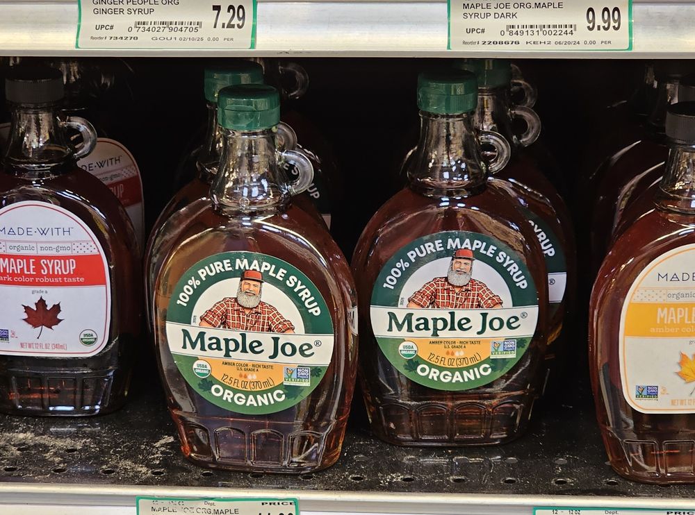 Grocery store shelf full of bottle of maple syrup, including Maple Joe brand. 