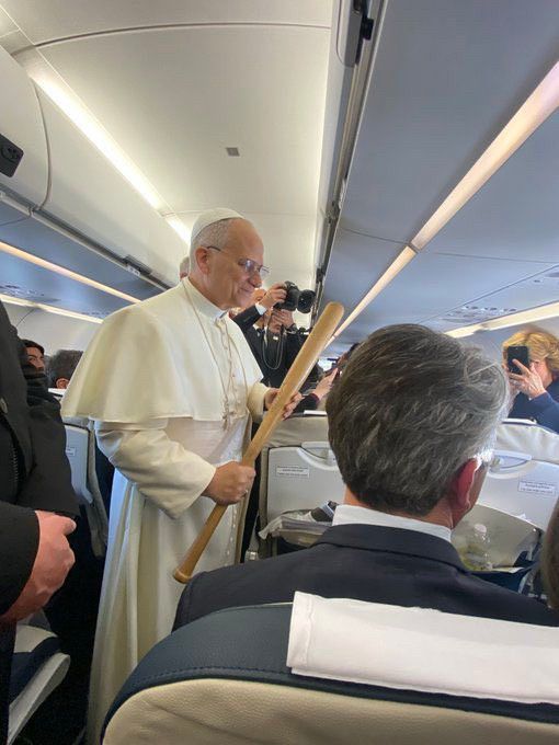 Pope on an airplane leaning over a seat with a baseball bat. He looks a bit severe.