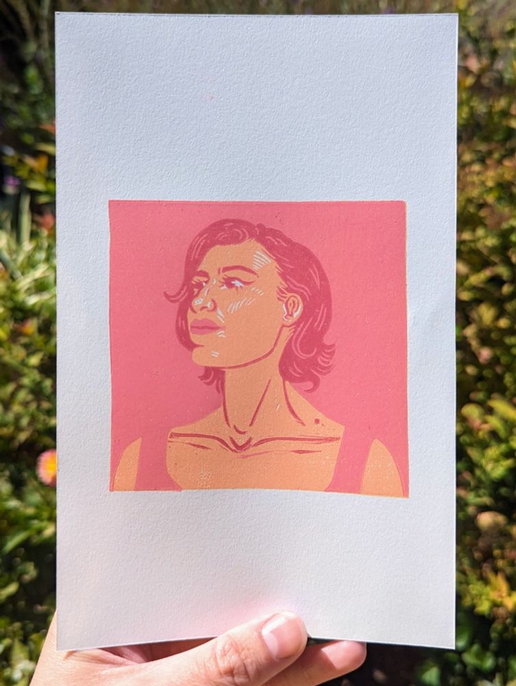 A rubber block print reduction portrait of a woman in various colors of orange and pink. Reference from RedditGetsDrawn.