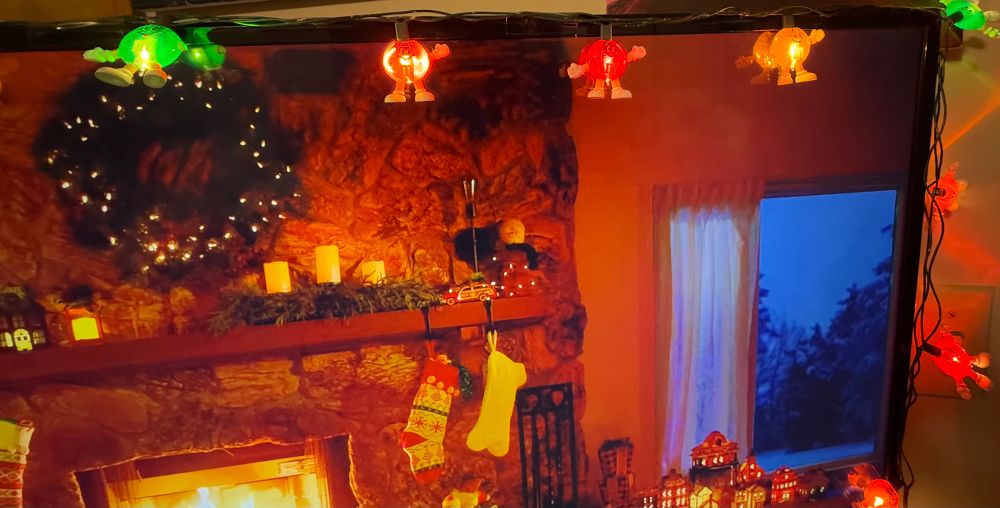 Roku cozy Christmas channel with M&M lights around the TV. 