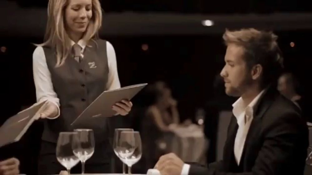 a woman in a vest with the letter n on it is serving a man in a suit