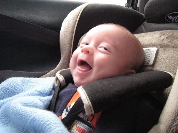 A baby laughing with joy as he wears the baby blue blanket in his car seat