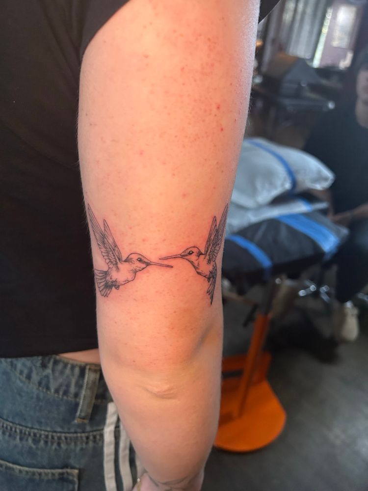 Dainty fineline tattoo of two hummingbirds facing each other