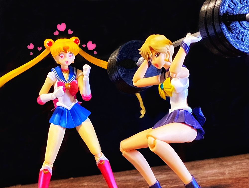 Magical girl in sailor outfit watching and cheering on another lifting a barbell with three weights on each side. 