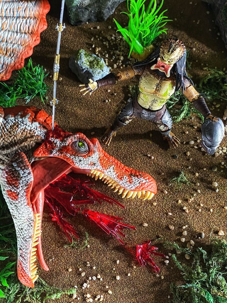 Alien hunter roaring in victory next to dead dinosaur head.