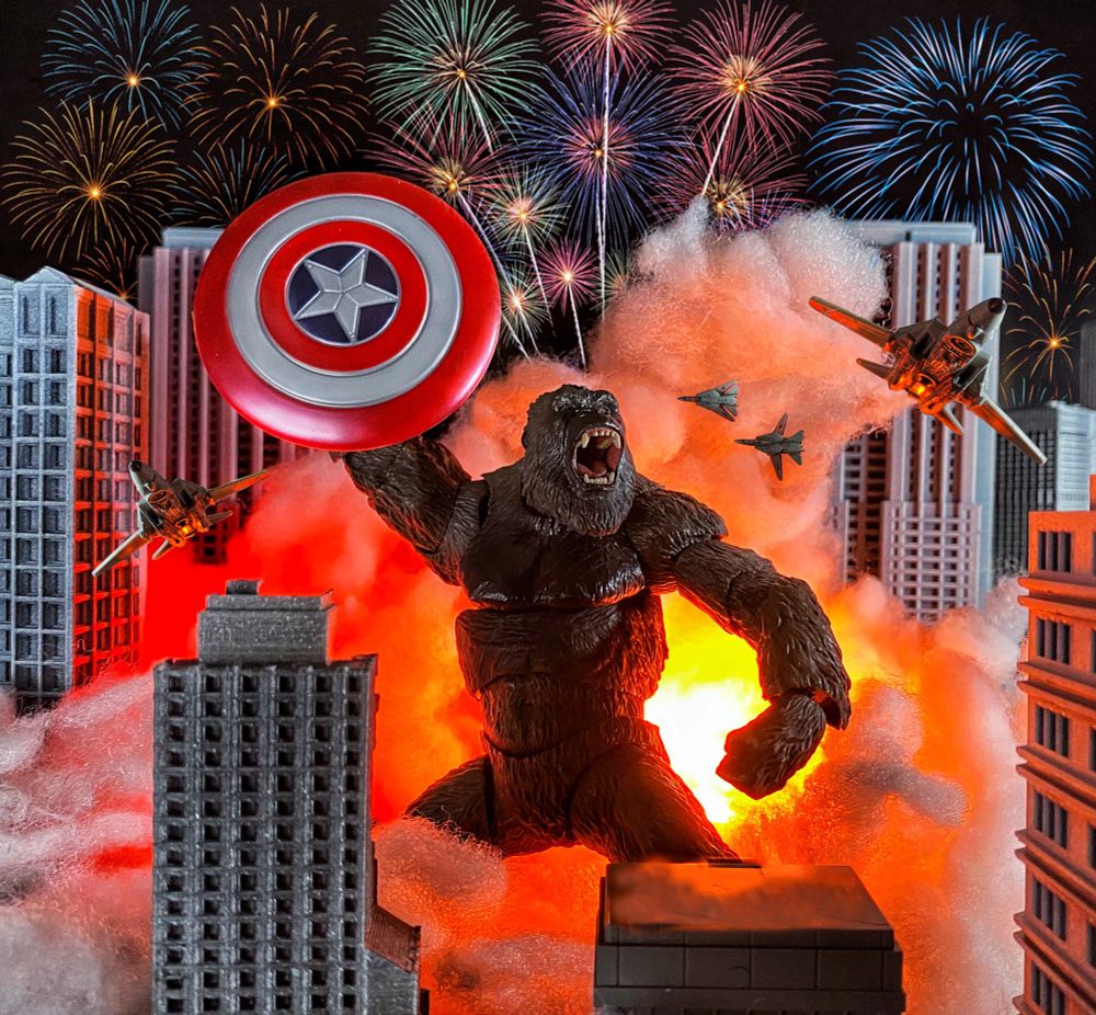 Giant ape roaring in the middle of the city while holding a shield in the air. Also with explosions behind him and fireworks in the night sky.