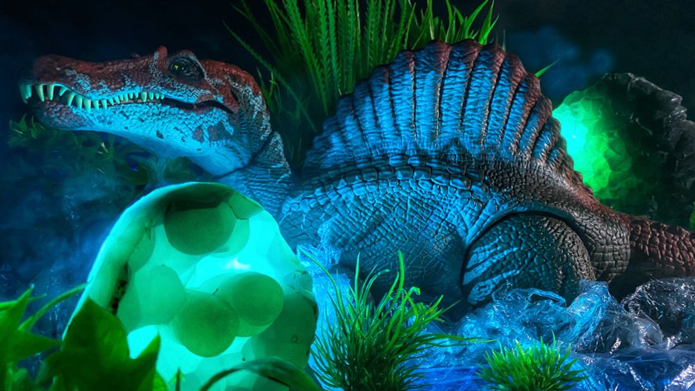 Dinosaur with sail on its back moving through water at night with glowing rocks on each side of it.