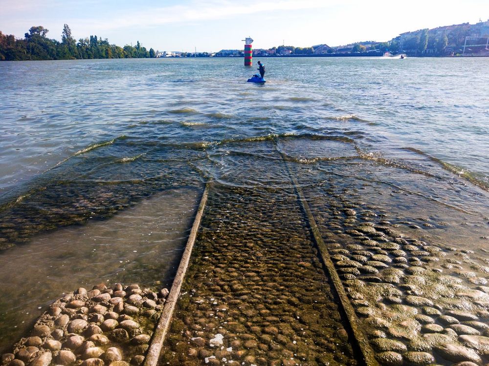 Confluence of Rhône and Saône in Lyon, with railway tracks disappearing into water and figure standing in waves.