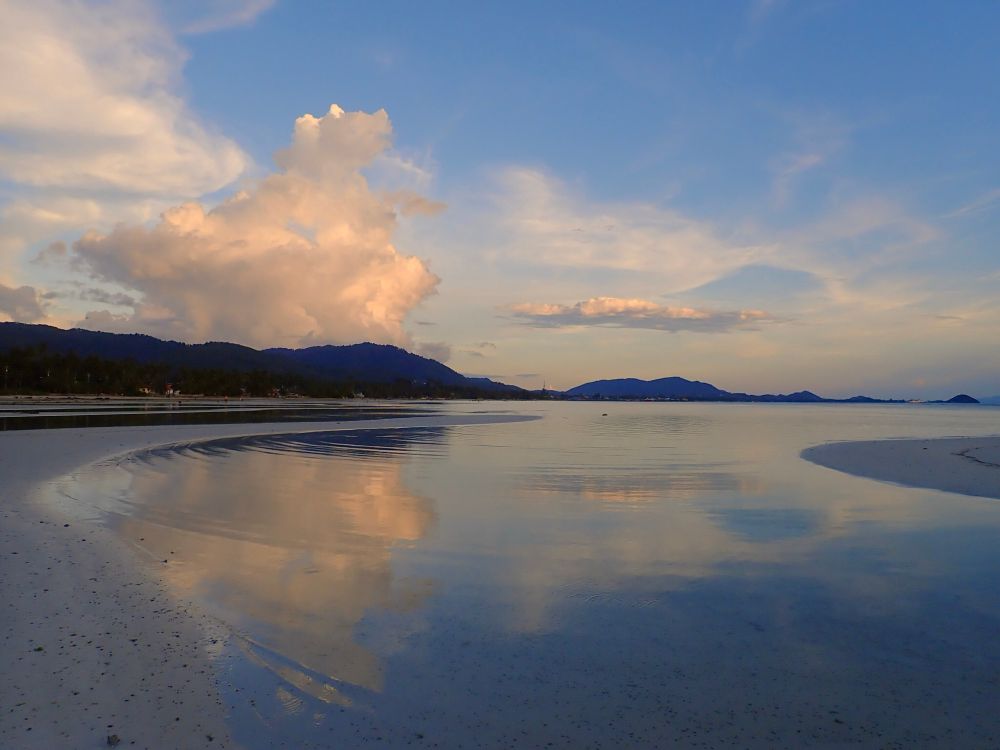 A photograph of an ocean Inlet with its shallow Stillwaters reflecting a blue and cloudy sky