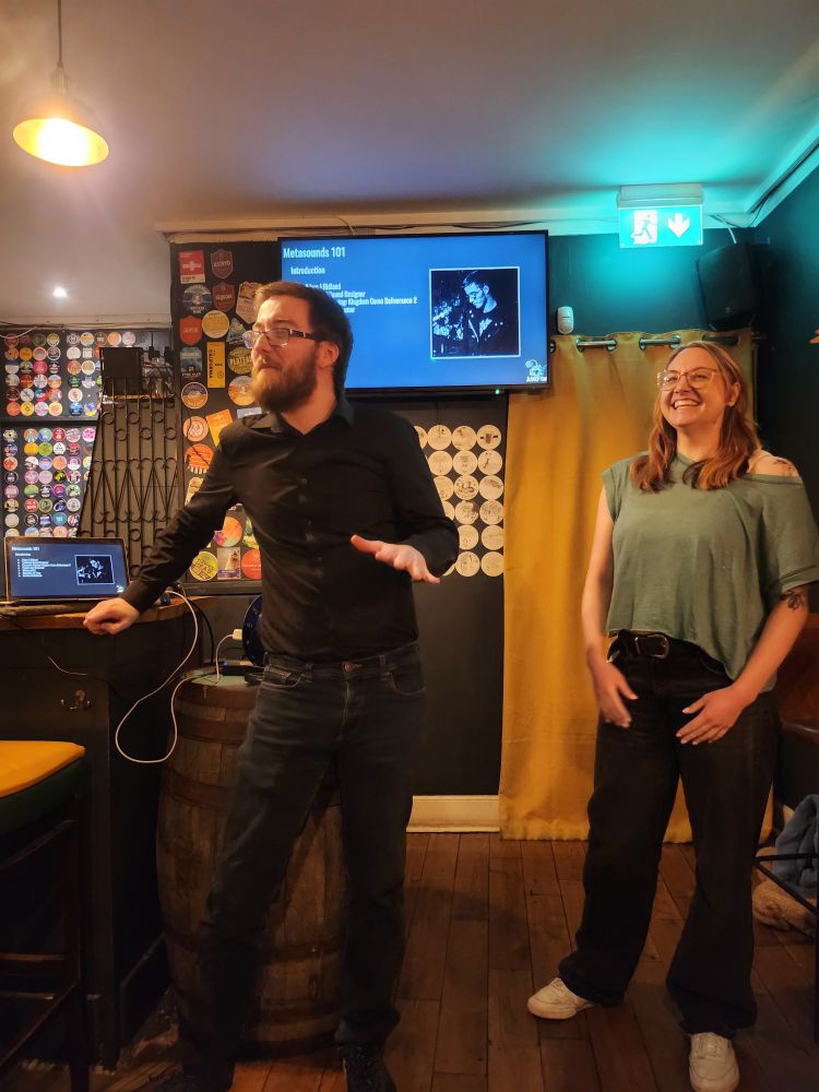 Adam on left, myself on right, presenting a talk on metasounds with tv in background in corner of pub. 