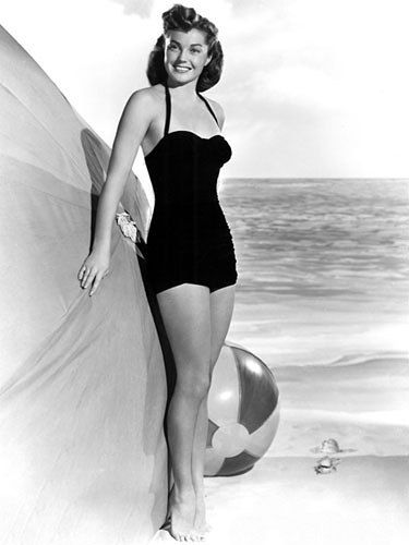 Esther Williams standing with beach ball and umbrella at the ocean