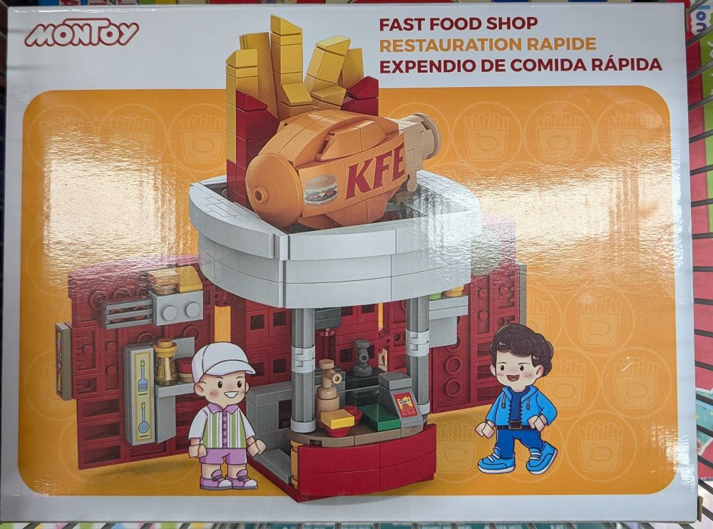 A Montoy fake Lego set of a chicken stand with the letters KFE on a giant drumstick on the top of the stand in front of some giant fries in a red holder.