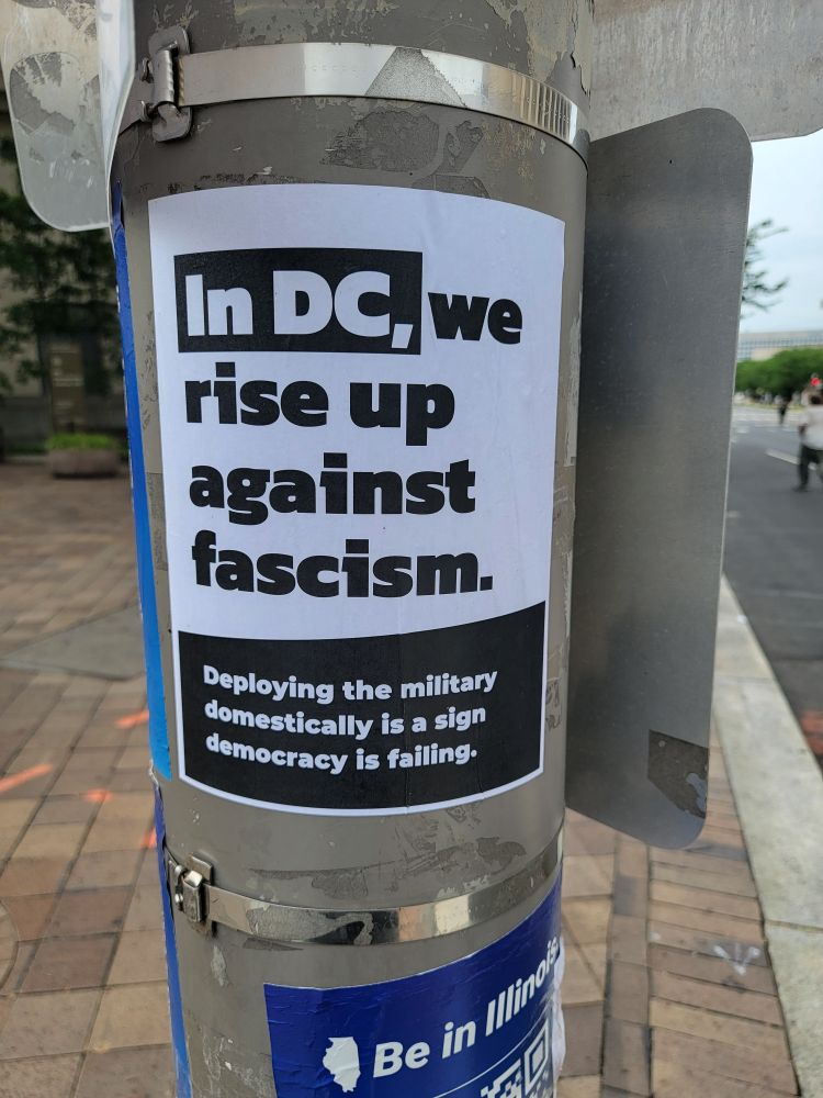 Autocollant en N&B sur un poteau
Sur fond noir "In DC,"
Sur fond blanc "we rise up against fascism."
Sur fond noir et en plus petite casse "Deploying the military domestically is a sign democraty is failing"
