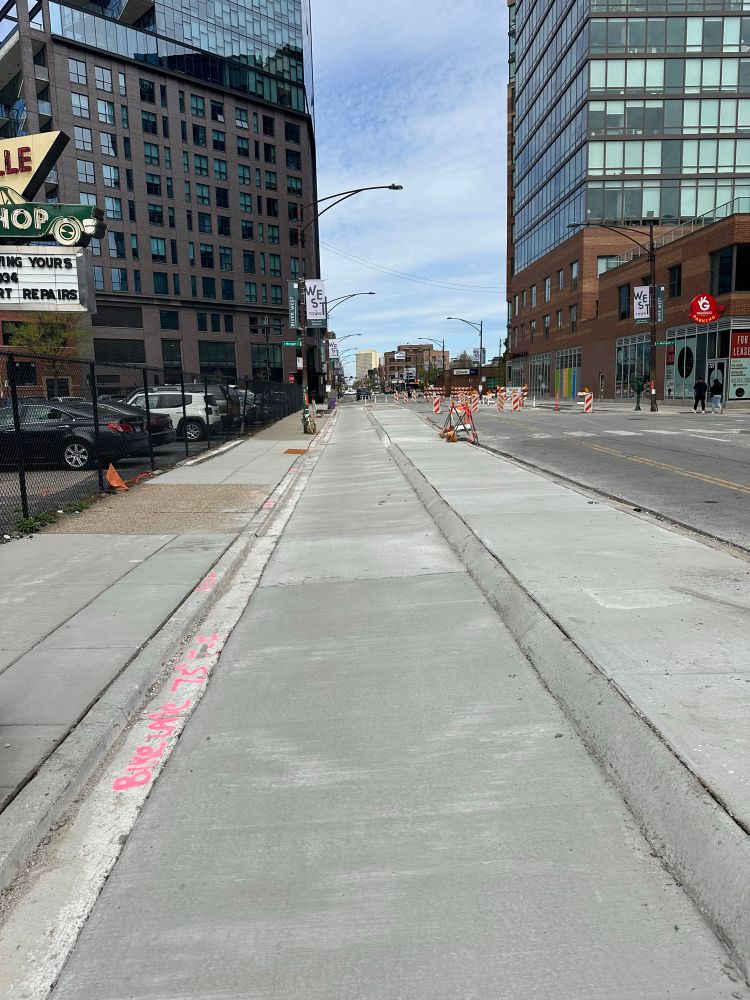 City street with a bike lane sandwiched between a sidewalk and protective cenent barrier