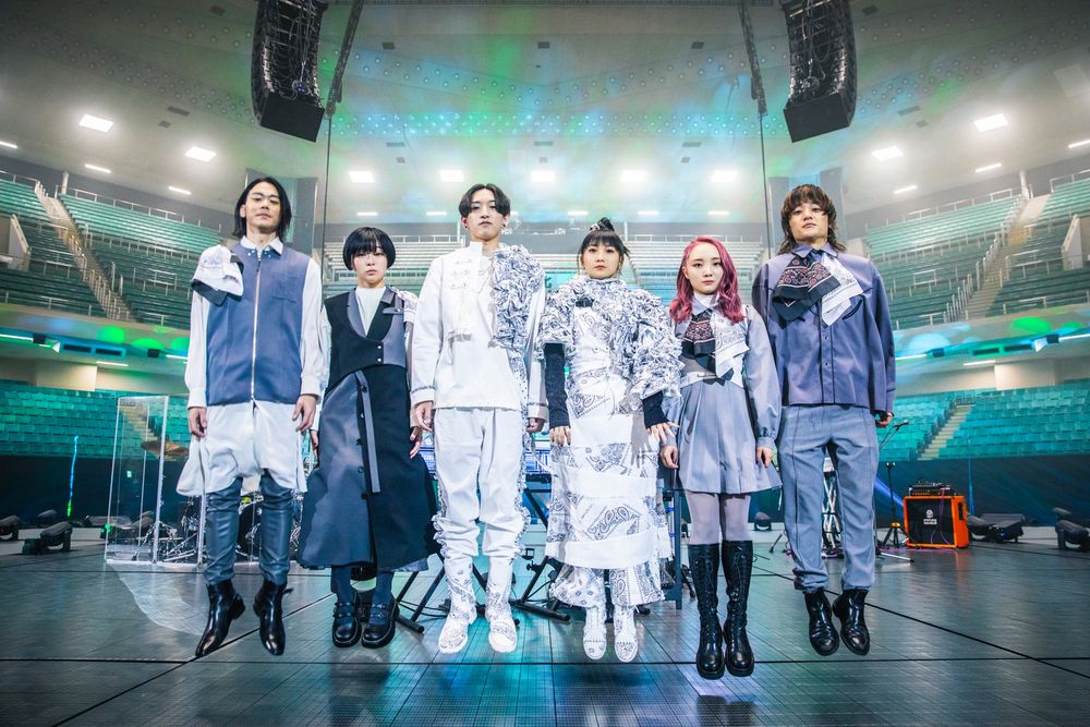 A photo of the Yoasobi live band jumping so all their feet are off the ground, but otherwise deadpanning 