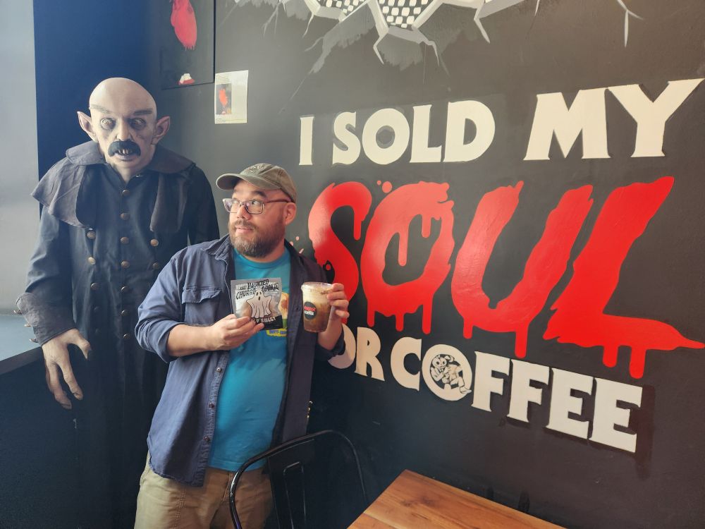 Posing in front of a mural with text that says "I sold my soul for coffee." A life-size figure of Nosterau from the 2024 Robert Eggers film adds atmosphere.
