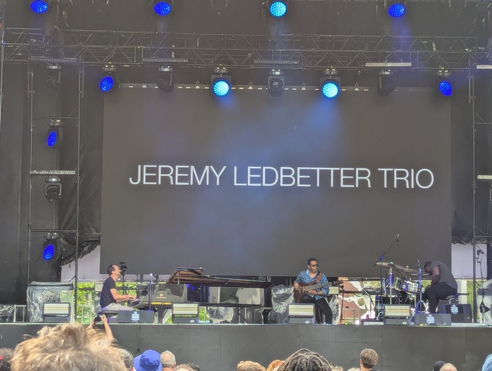 The Jeremy Ledbetter trio plays on an outdoor stage. 