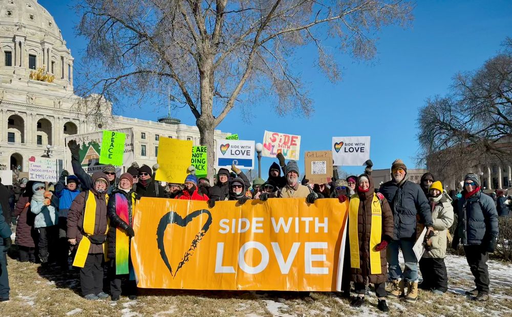 a group of people standing behind a side with love banner at the minnesota state capitol