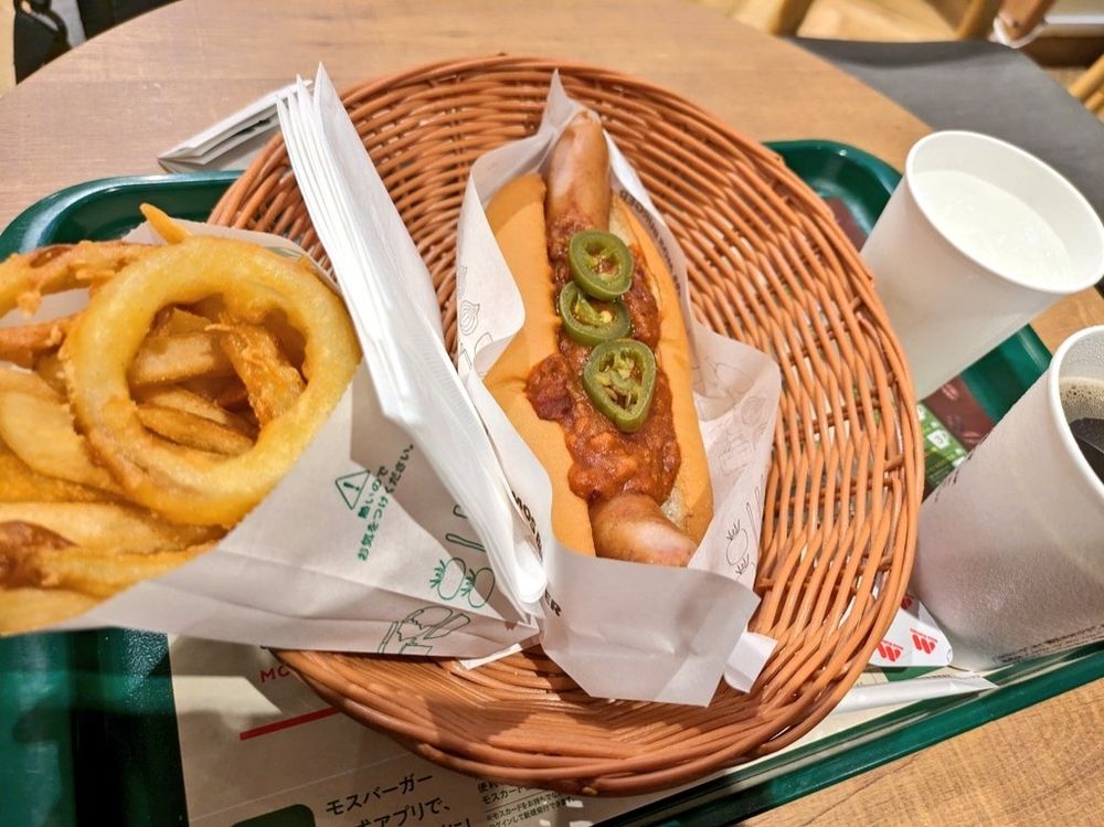 左端にオニオンリングとポテト。中央にスパイシーチリドッグ。チリドッグにハラペーニョのスライスが3枚乗せてある。右端に水とホットコーヒー。